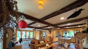 A rustic interior with a wooden ceiling, a dining area, a kitchen, and a living room with a sofa and coffee table.