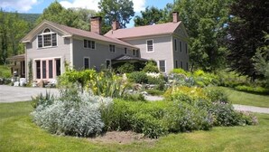 A two-story house with a front porch, surrounded by a well-maintained garden with various plants and flowers.