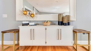 A white console with gold handles, a large mirror above, and two wooden side tables.