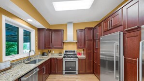 A kitchen with wooden cabinets, stainless steel appliances, a granite countertop, and a window with a view of greenery.