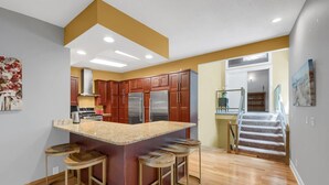A modern kitchen with a central island, wooden stools, and stainless steel appliances.