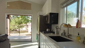 A modern kitchen with white cabinets, a stainless steel sink, and a window providing natural light. - Custom Palm Desert Casita, perfect desert location (Palm Desert)