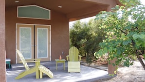 A covered outdoor area with two yellow Adirondack chairs, a small table, and a door with frosted glass panels. - Custom Palm Desert Casita, perfect desert location (Palm Desert)