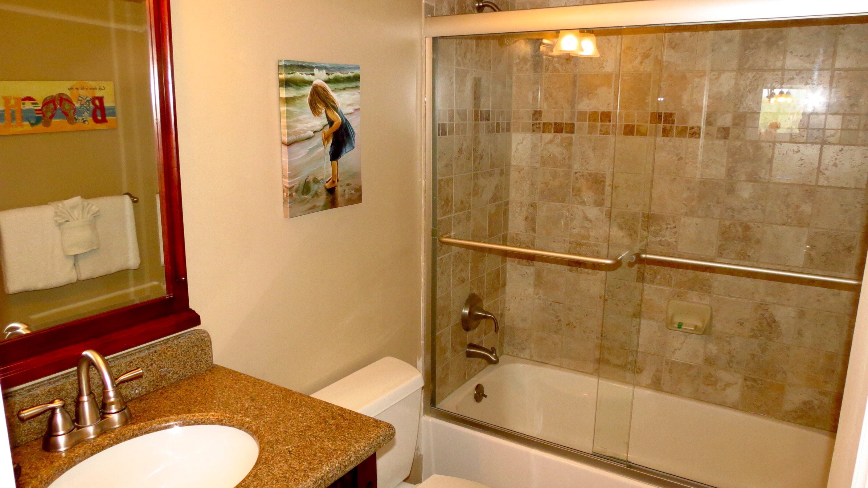 A bathroom with a sink, mirror, and glass-enclosed shower with grab bars.