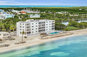 Hotel frente a la playa con piscina, varios balcones y vistas al océano y al puerto deportivo.