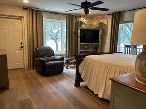 A bedroom with a bed, a leather chair, a television, and a ceiling fan.