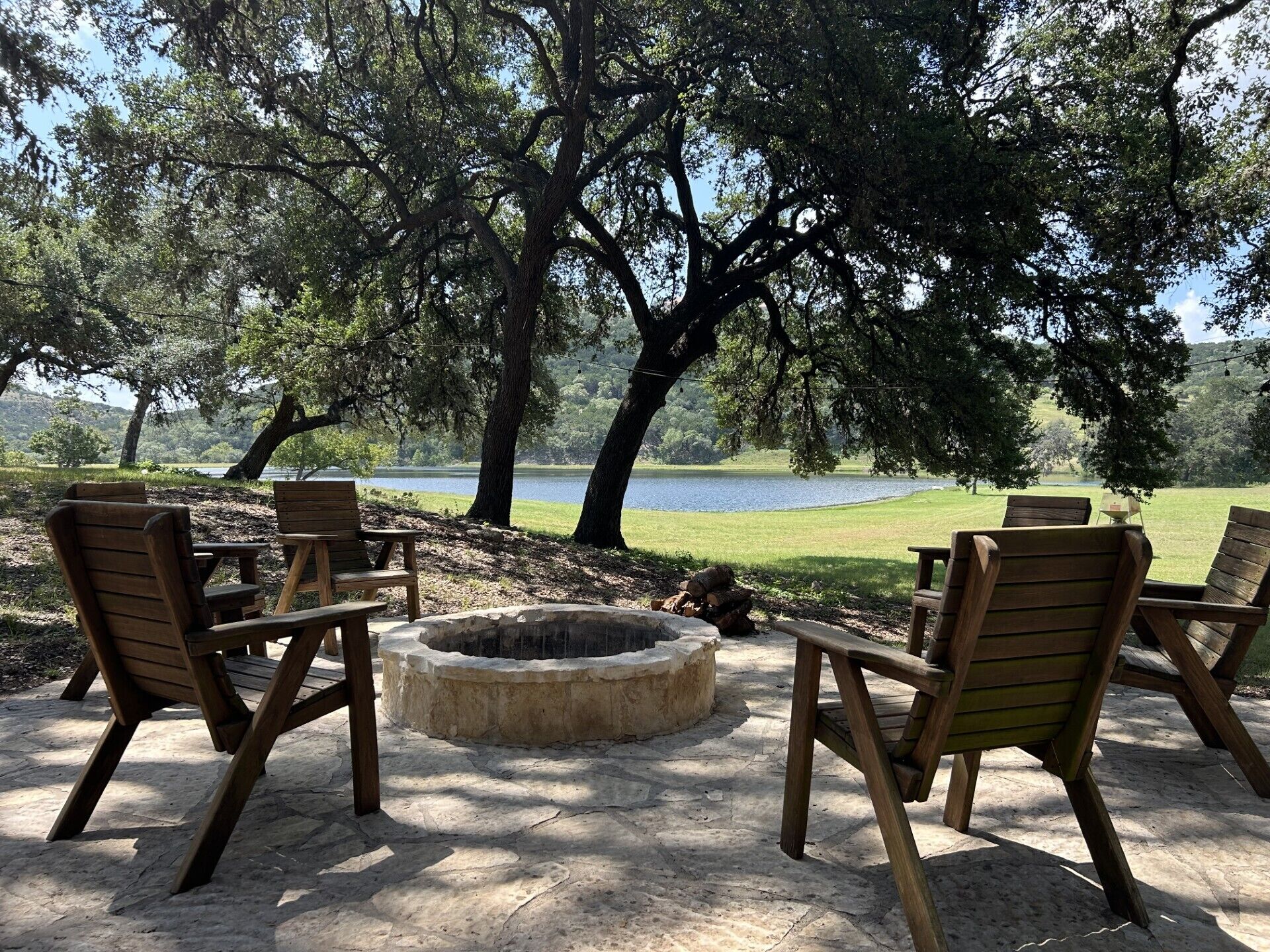 An outdoor seating area with wooden chairs and a fire pit, overlooking a lake.