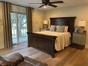 A bedroom with a large bed, two bedside tables, a ceiling fan, and a view through a sliding glass door.