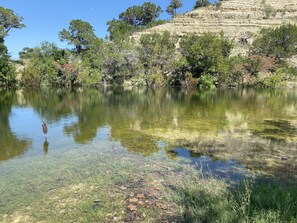 Ein klarer See mit Spiegelungen der umliegenden Bäume und einer felsigen Klippe.