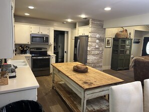 A modern kitchen with white cabinetry, a wooden dining table, and a stone accent wall.