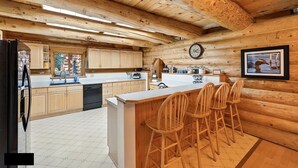 A spacious kitchen with wooden cabinetry, a central island with bar stools, and a clock on the wall. - Bear Paw Lodge : Custom-built log home only 4 miles from downtown Seward! (Seward)