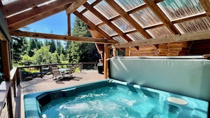 A hot tub with a wooden deck and glass ceiling, surrounded by trees. - Bear Paw Lodge : Custom-built log home only 4 miles from downtown Seward! (Seward)