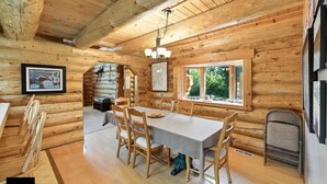 A wooden cabin interior with a dining table, chairs, a chandelier, and a fireplace. - Bear Paw Lodge : Custom-built log home only 4 miles from downtown Seward! (Seward)