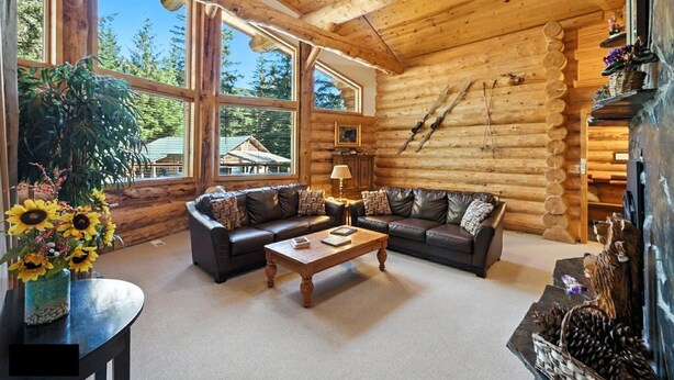 A log cabin interior with a large window, a sofa, a coffee table, and a ceiling fan. - Bear Paw Lodge : Custom-built log home only 4 miles from downtown Seward! (Seward)