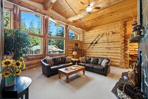 A log cabin interior with a large window, a sofa, a coffee table, and a ceiling fan. - Bear Paw Lodge : Custom-built log home only 4 miles from downtown Seward! (Seward)