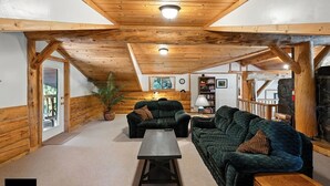 A cozy log cabin interior with a wooden ceiling, two sofas, a coffee table, and a stone fireplace. - Bear Paw Lodge : Custom-built log home only 4 miles from downtown Seward! (Seward)