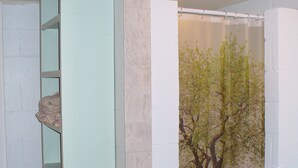 Un bany amb cortina de dutxa amb un dibuix d'un arbre, un envàs blanc i un moble prestatge amb una tovallola.