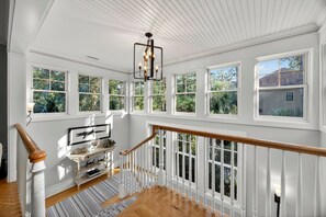 A spacious room with large windows, a wooden staircase, and a chandelier.