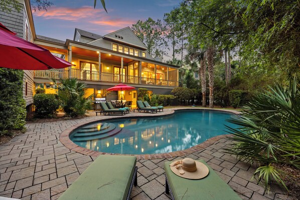 A house with a swimming pool, outdoor furniture, and a well-lit porch.