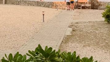 A beachside walkway leading to a thatched-roof structure, a stone wall, and a bench.