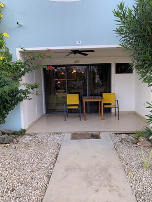 A covered patio area with two yellow chairs and a table, a ceiling fan, and a door leading to an interior space.