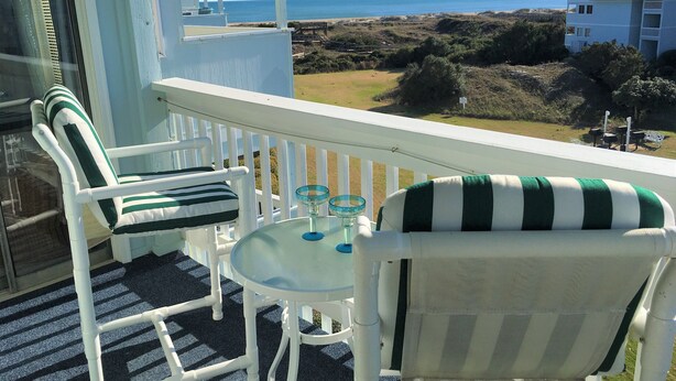 Ein Balkon mit weißen Stühlen und einem Tisch mit Blick auf einen Strand und das Meer.