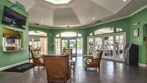 A spacious lobby with wicker furniture, a reception desk, and a fitness area with exercise equipment. - Florida Winter Escape 🌴 6BR Private Pool Snowbird + Family Visits (Kissimmee)