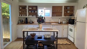 Una cocina con armarios blancos, una isla central con taburetes y vistas a través de una puerta corrediza de cristal.