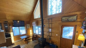 A cozy cabin interior with a wooden interior, a fireplace, a television, and a dining area.