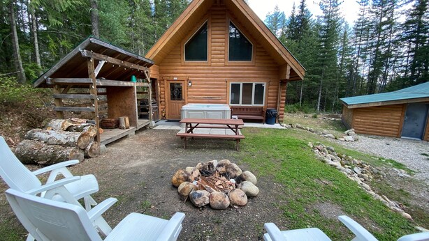 A wooden cabin with a fire pit, picnic table, and outdoor seating.