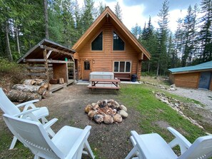 Une cabane en bois avec un foyer, une table de pique-nique et des sièges d’extérieur.