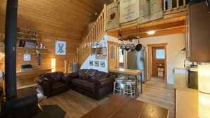 A cozy wooden interior with a leather sofa, a dining table, and a kitchen area with a refrigerator and hanging pots.