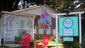 Une charmante maison de campagne avec une façade en bois, une clôture en treillis et deux chaises rouges devant la porte.