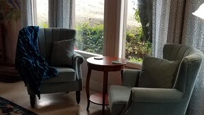 Un salon chaleureux avec deux fauteuils, une petite table ronde et une grande fenêtre avec des rideaux.