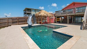 Una piscina con una estructura de techo de paja, un tobogán y una terraza de madera.