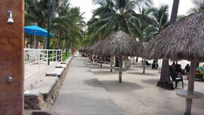 Un paseo marítimo en la playa con sombrillas de paja y palmeras.
