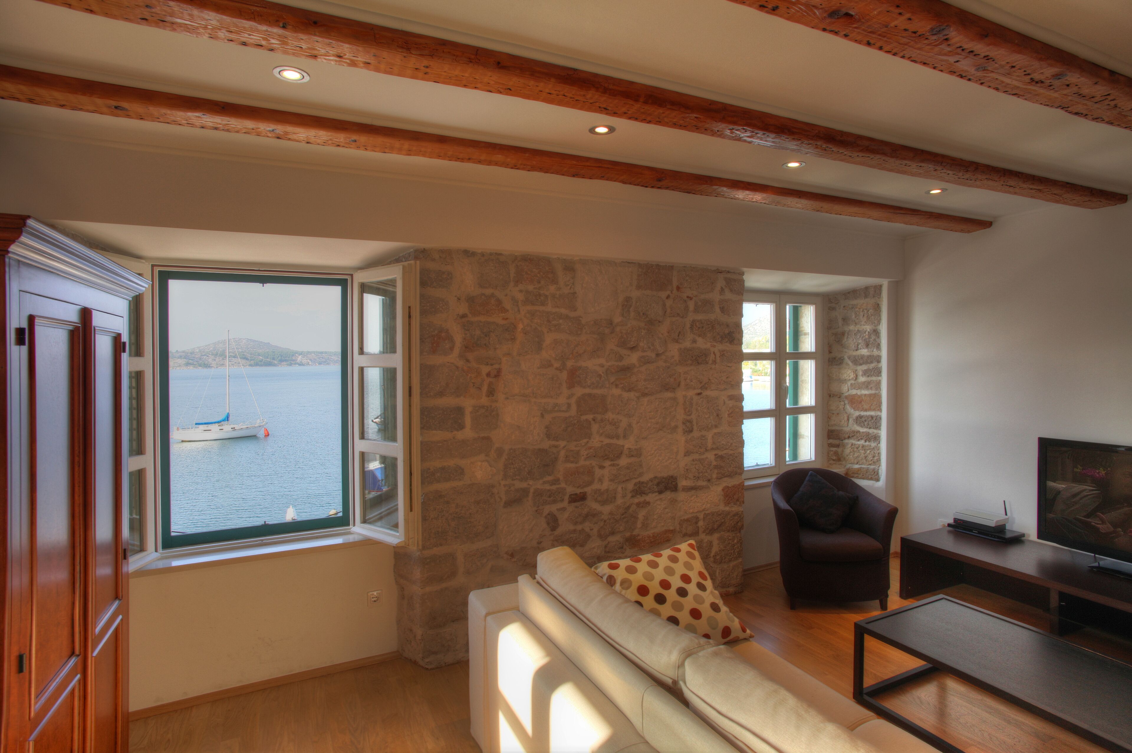 A living room with a stone wall, wooden beams, a sofa, a chair, and a television.
