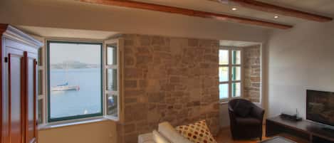 A living room with a stone wall, wooden beams, a sofa, a chair, and a television.