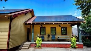A yellow house with a red roof, a covered porch with two chairs and a table, and solar panels on the roof. - Your Next 5 Star Get Away! (Little Rock)