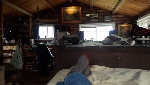 L’intérieur d’un chalet rustique, avec un lit, des murs en bois, une fenêtre et un tableau accroché au mur.