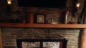 Une cheminée en pierre avec un manteau en bois, un tapis et une petite table sur laquelle est posée une bougie.