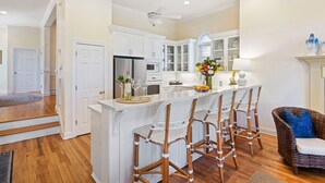 A kitchen with white cabinets, a central island with bar stools, a refrigerator, and a microwave. - Ideal Ocean Point Location- Close to Pool + Beach (Isle Of Palms)