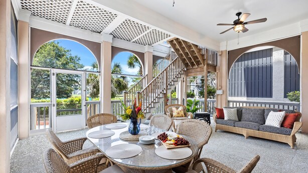 An outdoor dining area with wicker furniture, a glass table, and a staircase leading to a balcony. - Ideal Ocean Point Location- Close to Pool + Beach (Isle Of Palms)