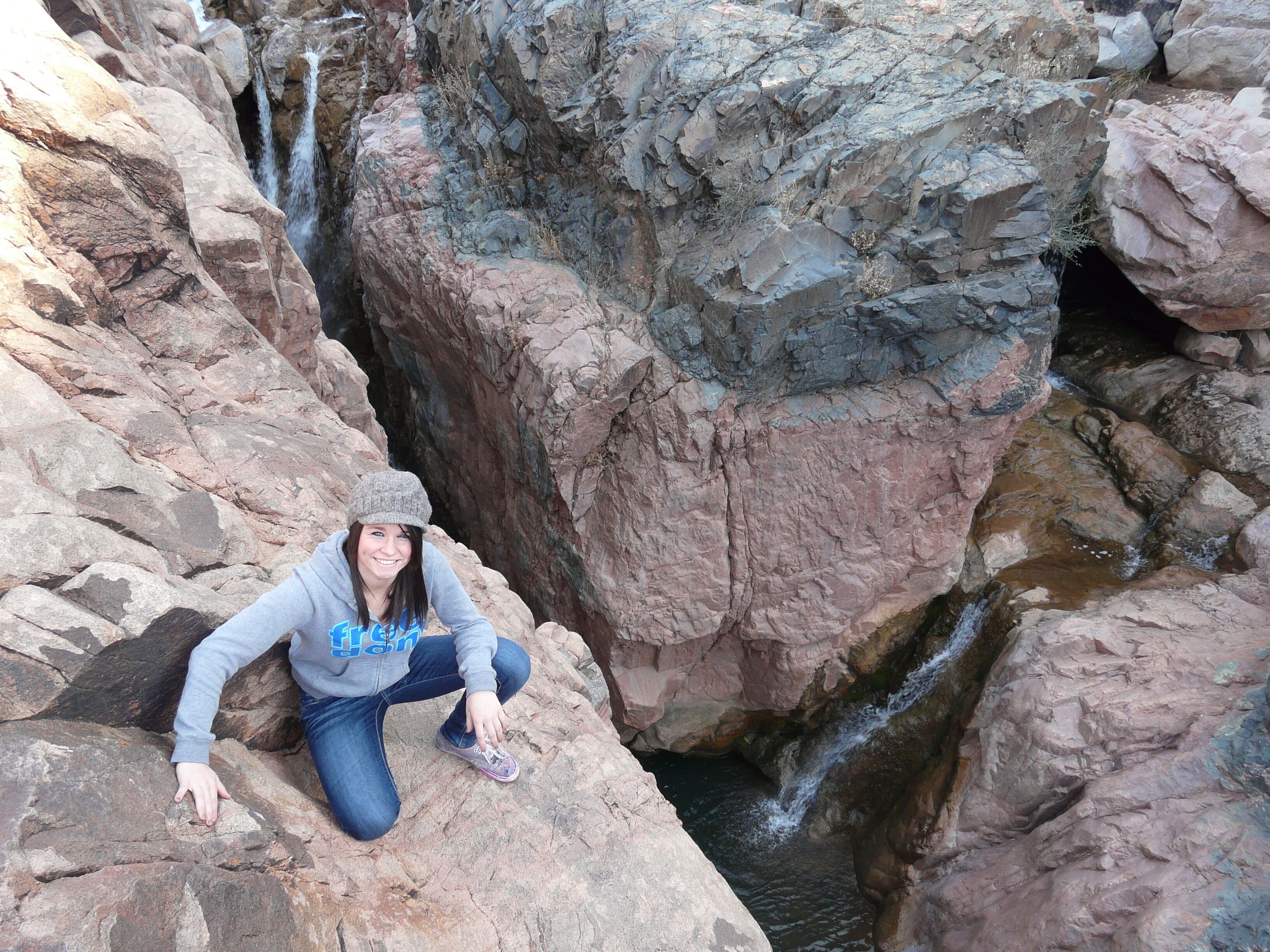 A person sitting on a rocky ledge with a waterfall in the background.
