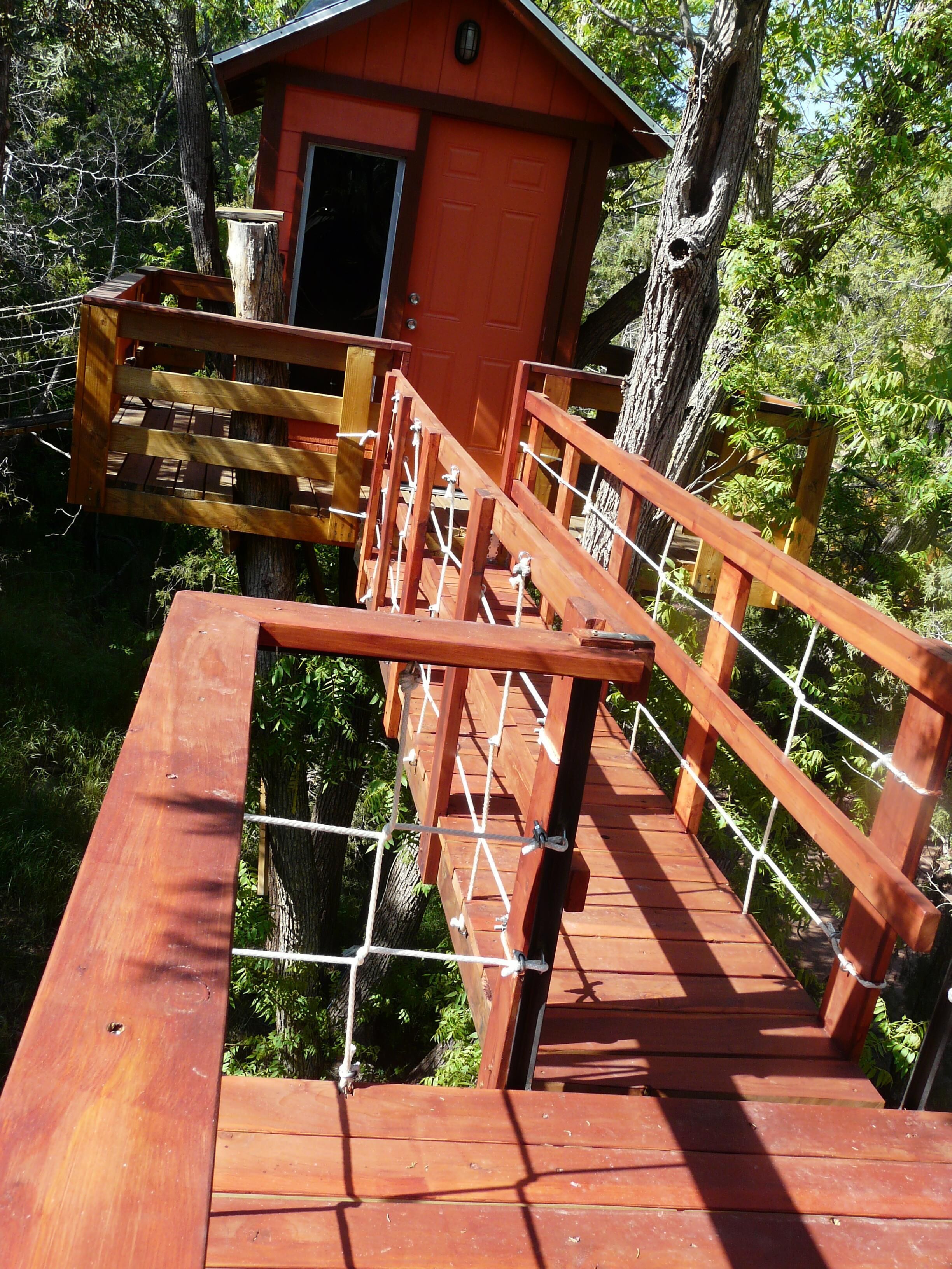 Un puente de madera que lleva a una pequeña cabaña roja en un área boscosa.