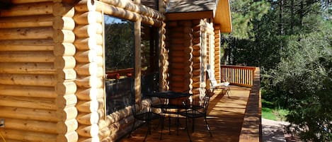 Une cabane en rondins dotée d’une terrasse, de meubles de jardin et offrant une vue sur la forêt environnante.