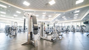 Une salle de sport spacieuse, dotée de divers appareils d’exercice, de grandes fenêtres et d’un plafond haut avec des luminaires encastrés.