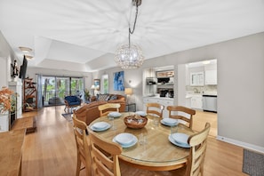 A modern dining area with a glass table, wooden chairs, and a chandelier.