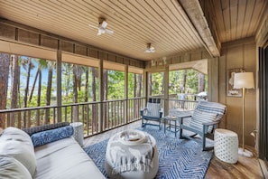 A covered outdoor area with a wooden ceiling, a sofa, a dining table, and chairs.