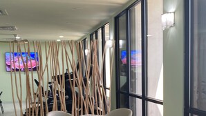 Un comedor moderno con mesas y sillas blancas, una pantalla de televisión y un panel decorativo de madera.